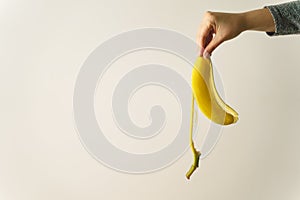 Hand of unknown caucasian woman holding banana peel in front of white wall - copy space concept of ending and finish trash ready