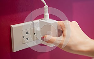 The hand unplugged the electric line off a white socket on the red wall.