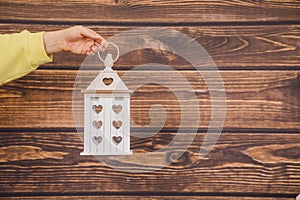 Human hand of an unrecognizable woman holds wooden lantern with hearts on a wooden background. concept of decor from natural