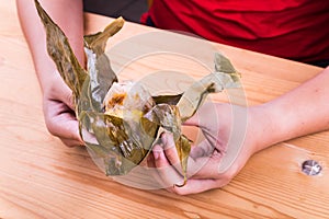 Hand unwrapping Chinese rice dumpling or zongzi on table