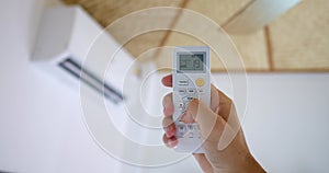 Hand uses remote activate air conditioner, lowering temperature button display comfort. effective against heat, ensuring