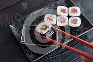 Hand using chopsticks pick. Maki-Sushi, tuna-maki rolls on a black stone plate. Fresh made Sushi set with tuna, cheese and cucumbe