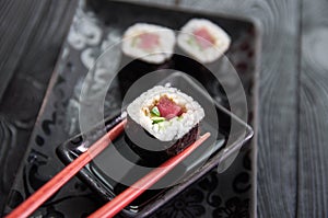 Hand using chopsticks pick. Maki-Sushi, tuna-maki rolls on a black stone plate. Fresh made Sushi set with tuna, cheese and cucumbe