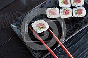 Hand using chopsticks pick. Maki-Sushi, tuna-maki rolls on a black stone plate. Fresh made Sushi set with tuna, cheese and cucumbe