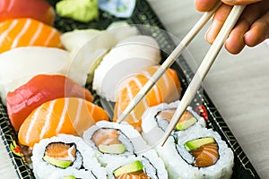 Hand using chopsticks pick Sushi, Sashimi and Futomaki rolls. Fresh made Sushi set with salmon, prawns, wasabi and ginger. Tradit