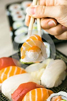 Hand using chopsticks pick Sushi, Sashimi and Futomaki rolls. Fresh made Sushi set with salmon, prawns, wasabi and ginger. Tradit