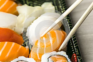 Hand using chopsticks pick Sushi, Sashimi and Futomaki rolls. Fresh made Sushi set with salmon, prawns, wasabi and ginger. Tradit