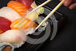 Hand using chopsticks pick. Sushi and Sashimi rolls on a black stone slatter. Fresh made Sushi set with salmon, prawns, wasabi and