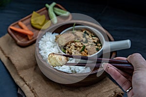 The hand is using chopsticks to pick up  Stir fried egg tofu with spring onion with Herbs vegetables served with steamed rice in