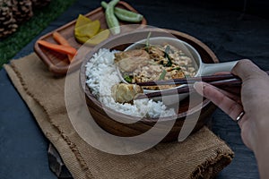 The hand is using chopsticks to pick up  Stir fried egg tofu with spring onion with Herbs vegetables served with steamed rice in