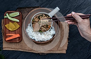 The hand is using chopsticks to pick up  Stir fried egg tofu with spring onion with Herbs vegetables served with steamed rice in