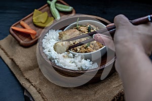 The hand is using chopsticks to pick up  Stir fried egg tofu with spring onion with Herbs vegetables served with steamed rice in