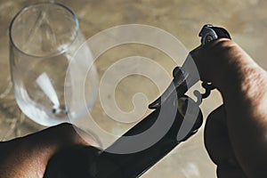 Hand using corkscrew to extract cork from a bottle and empty wine glass