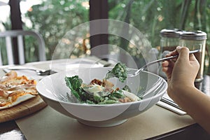 A hand using fork to scoop up Ceasar salad to eat with pizza on dining table