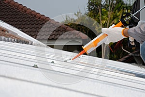 hand using glue gun or caulking gun on the roof. photo