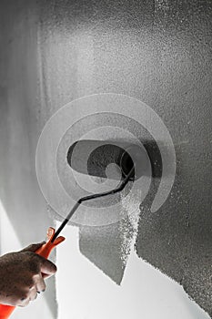 Hand using paint roller applying grey paint on white wall.