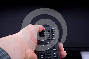 Hand using a remote control in front of the TV screen