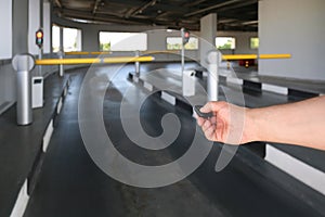 A hand using a remote control opens an automatic barrier in a parking lot. Raising the barrier when leaving the parking