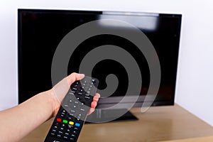 Hand using a remote control to turn off on on the TV with an empty screen