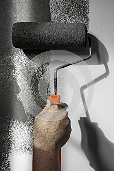 Hand using roller paint applying grey paint on white wall.