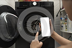 Hand using smartphone app to control front load washing machine, blank white screen for smart home concept