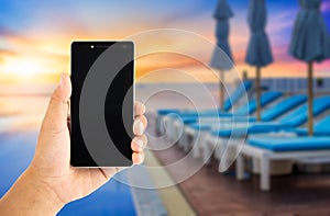 hand using smartphone with view sunrise of swimingpool