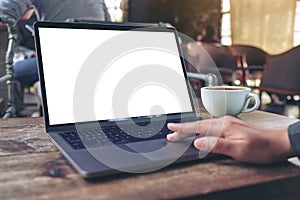 A hand using and touching at laptop touchpad with blank white desktop screen with coffee cup on wooden table in cafe