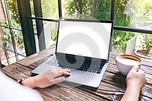 A hand using and touching on laptop touchpad with blank white desktop screen while drinking coffee