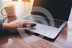 A hand using and touching on laptop touchpad with coffee cup on wooden table