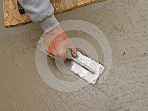 Hand using trowel to finish concrete slab