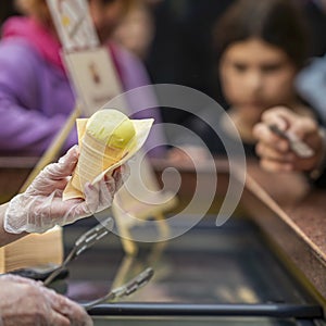 Hand Of Vendor Holding fruit Ice Cream Cone, background of counter with sweet dessert. Real scene in store