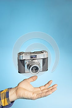 Hand with a vintage camera suspended in the air on a light blue background. Photography day concept