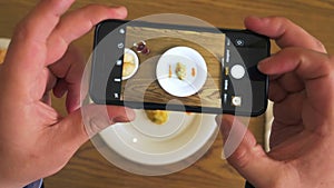 Hand waiter places dish with food and man using mobile phone for photo topview