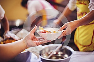 The hand of the wanderer extends to receive food from donations. With volunteers scooping food: the idea of helping with hunger