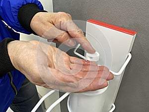 Hand washing with disinfectant close-up. Elderly woman disinfects her hands with an antiseptic gel automatic dispenser