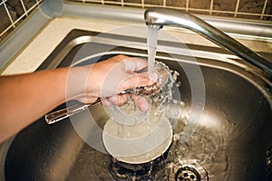 hand washing spoon under the tap in the sink. the plate is blurred