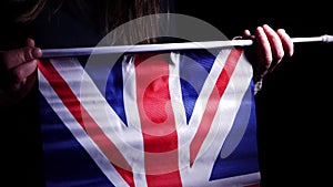 Hand waving British Union Jack flag on dark background