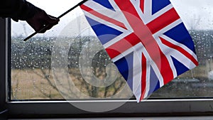 Hand waving British Union Jack flag on rainy day