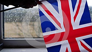 Hand waving British Union Jack flag on rainy day