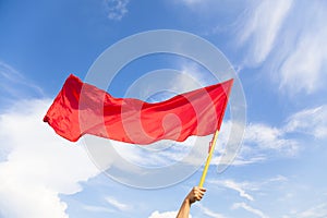 Hand waving a red flag with blue sky background