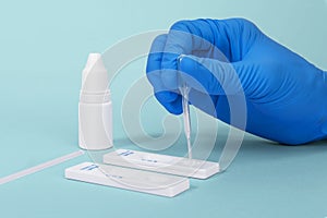 Hand wearing blue surgical gloves, placing the sample into the covid-19 antigen diagnostic test device, on  blue background