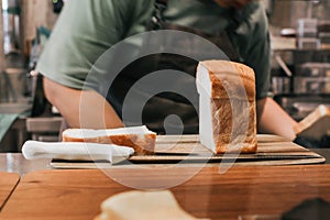 Hand wearing glove with a knife cuts loaf of bread on a wooden board.