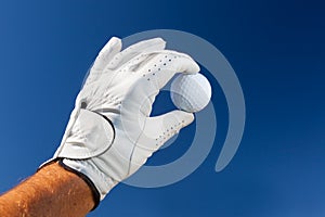 Hand wearing golf glove holding a white golf ball