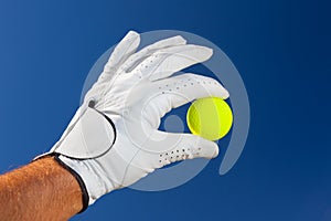 Hand wearing golf glove holding a yellow golf ball