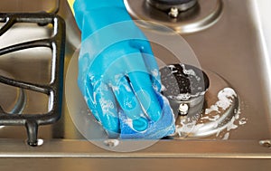 Hand wearing rubber glove while cleaning stove top range with s