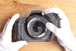 Hand wearing white gloves cleaning camera with air dust blower