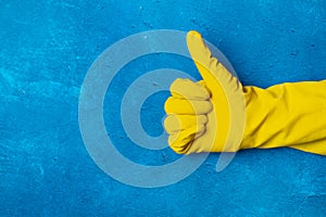 A hand wearing a yellow cleaning glove with thumb up on a blue background