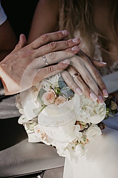 A hand of wedding couple touch each other over wedding bouquet. Hands newlyweds with wedding rings close up. Bridal hands with