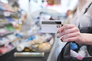 Hand with a white credit card on the background of a supermarket cash desk