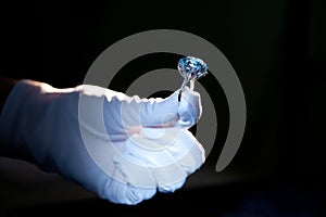 Hand in white glove holding precious metal ring with big blue gem